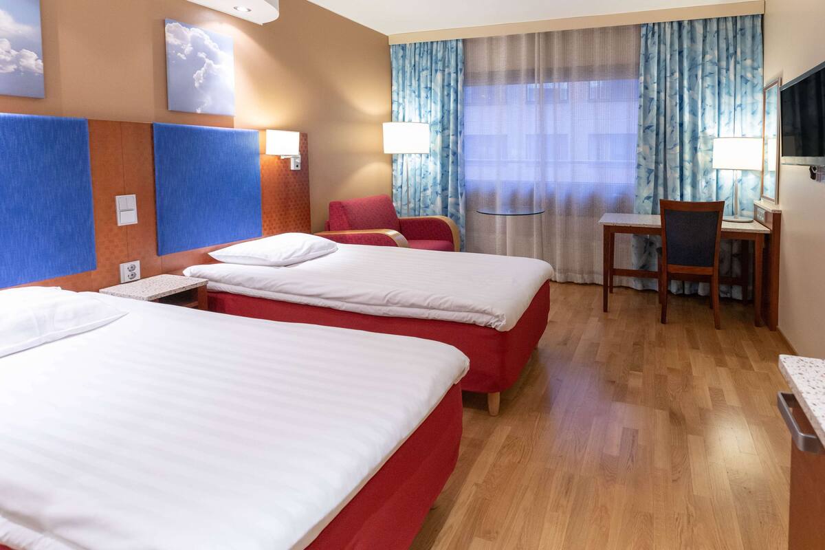 Habitación de hotel con dos camas, un escritorio, una silla y un televisor.