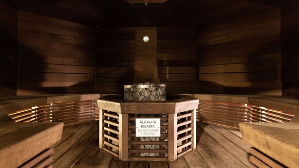 Un sauna doté d’un bassin en pierre et d’un panneau indiquant qu’il ne faut pas recouvrir le poêle.