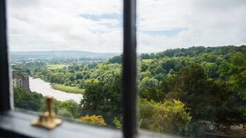 Une vue depuis une fenêtre donnant sur une rivière, entourée d’une végétation luxuriante et avec, au loin, le paysage urbain.