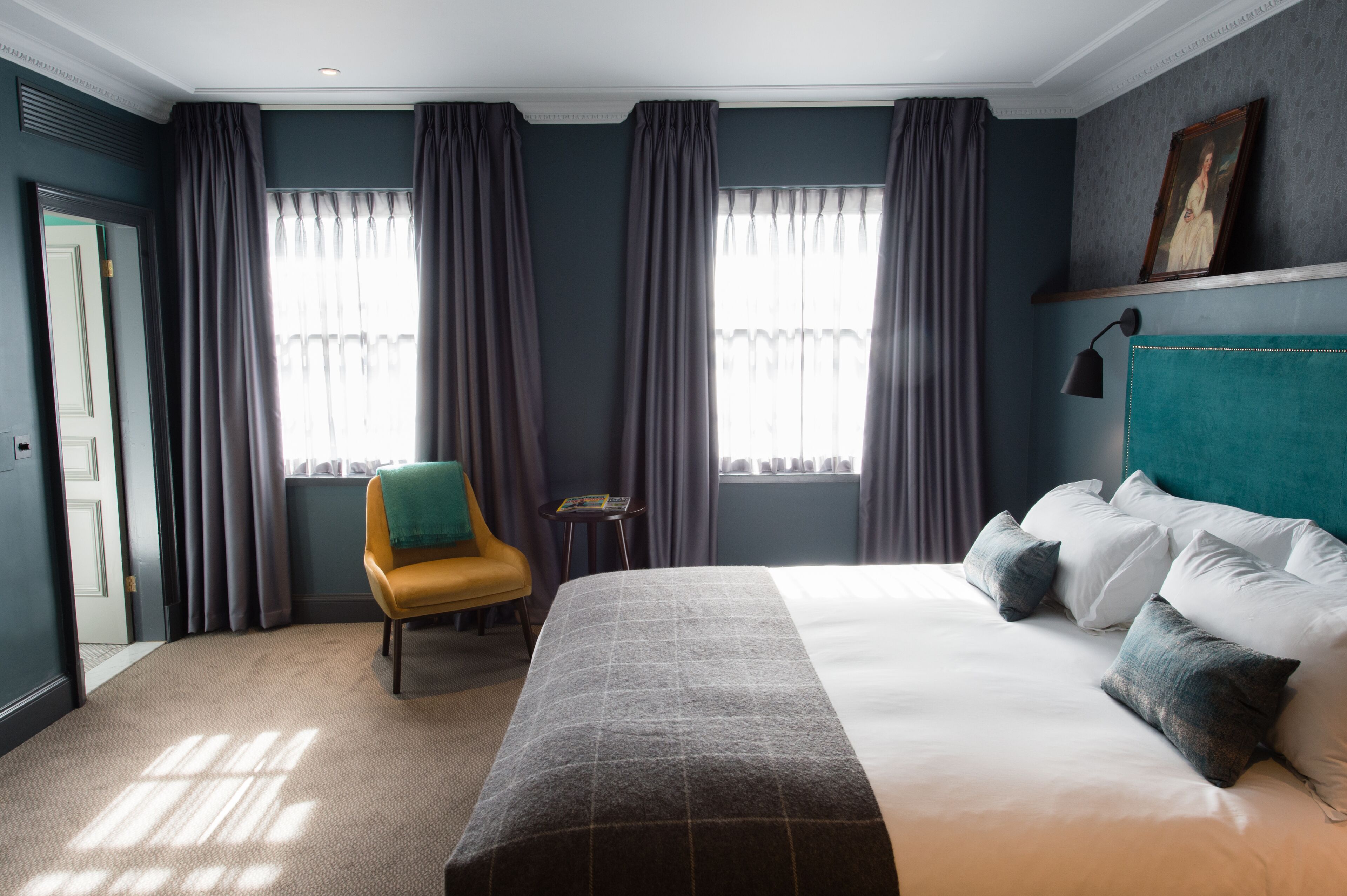 A hotel room with a large bed, a chair, a small table, and a painting on the wall.