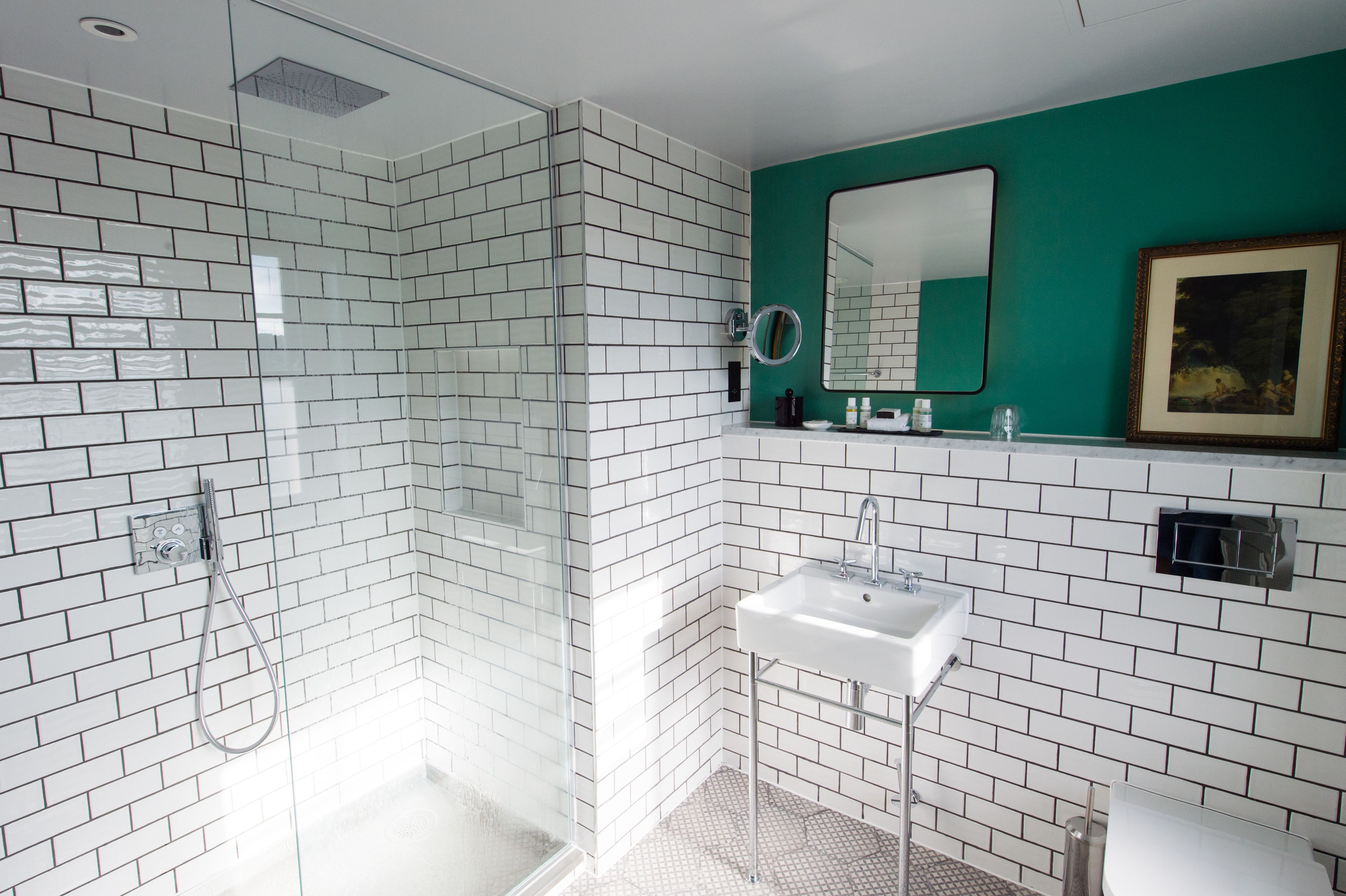 Un baño moderno con azulejos blancos tipo metro, ducha con cerramiento de vidrio, lavamanos blanco y pared de acento verde.