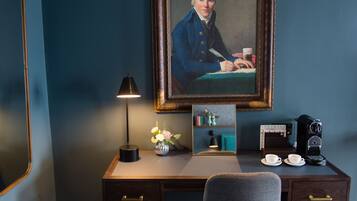 A desk with a framed portrait, a lamp, a vase with flowers, a coffee maker, and two cups.