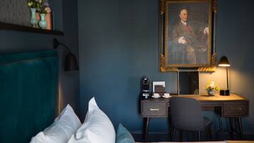 Una camera d'albergo con un letto, una scrivania con un computer, una lampada e un ritratto incorniciato appeso al muro.