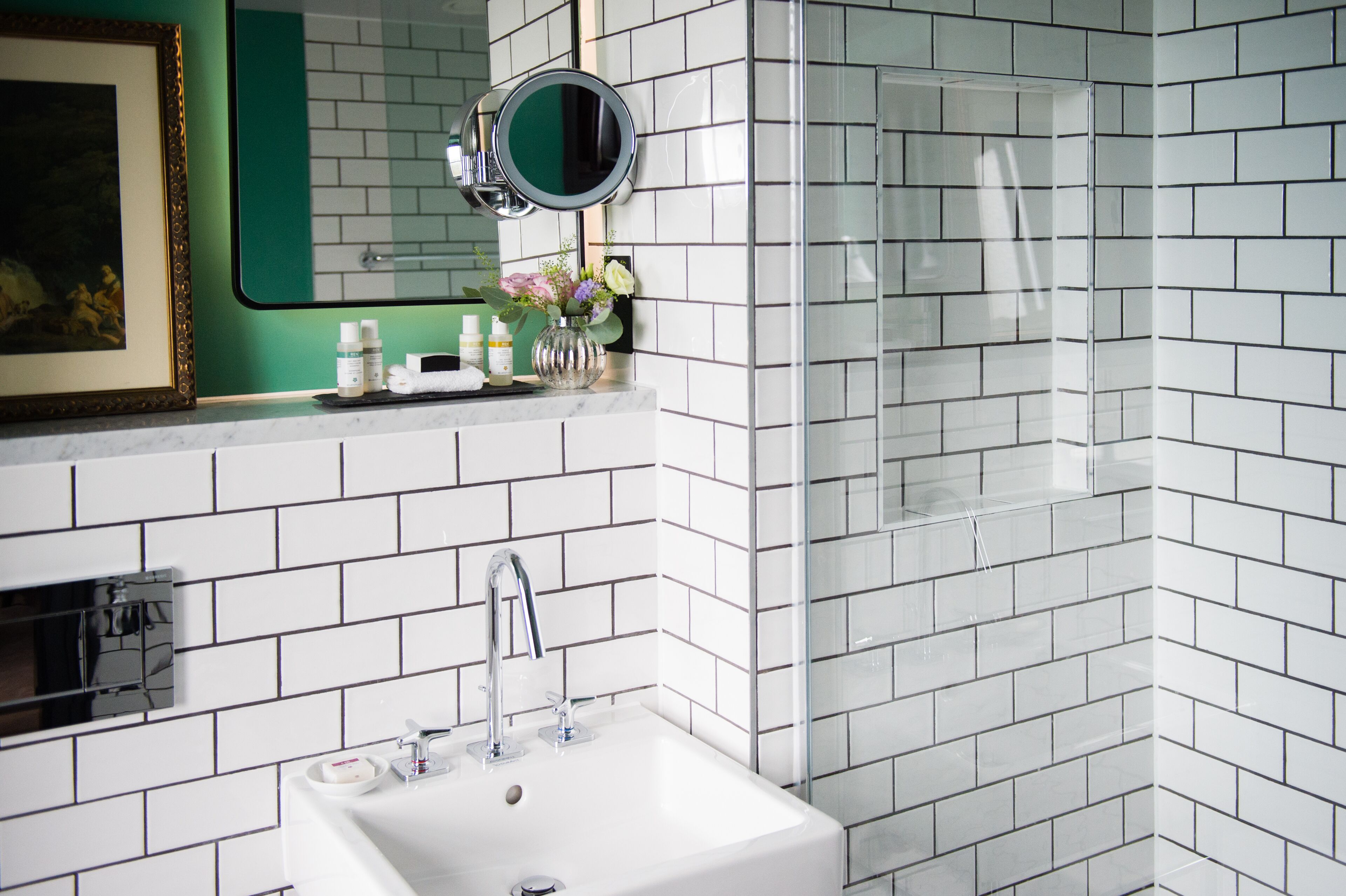 Ein Badezimmer mit weißen Fliesen im U-Bahn-Stil, einem Waschbecken mit Spiegel und einer Duschkabine.
