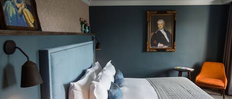 Ein Hotelzimmer mit einem großen Bett, einem Nachttisch, einer Leselampe, einem gerahmten Gemälde und einem orangefarbenen Sessel.