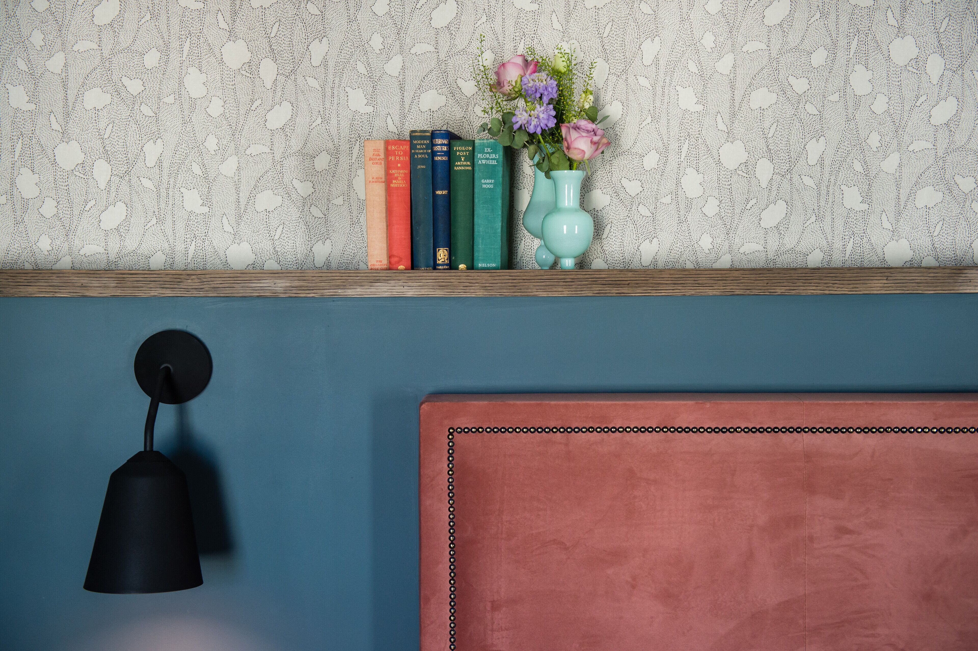 A bookshelf with books and a vase of flowers against a patterned wall.