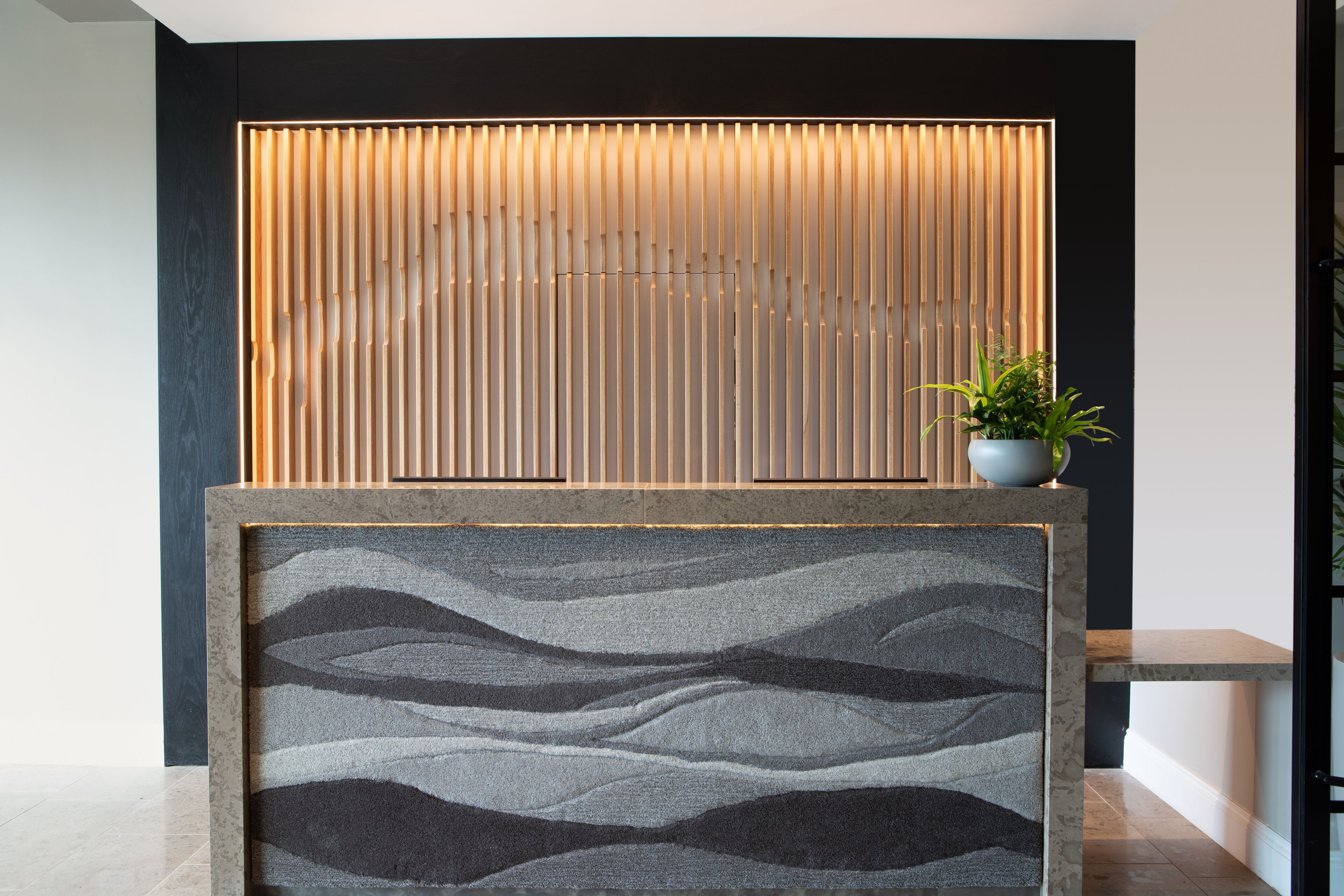 A reception area with a modern design, featuring a vertical wooden panel and a textured wall panel.