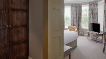 A bedroom with a large wooden door, a bed, a chair, a TV, and a window with curtains.