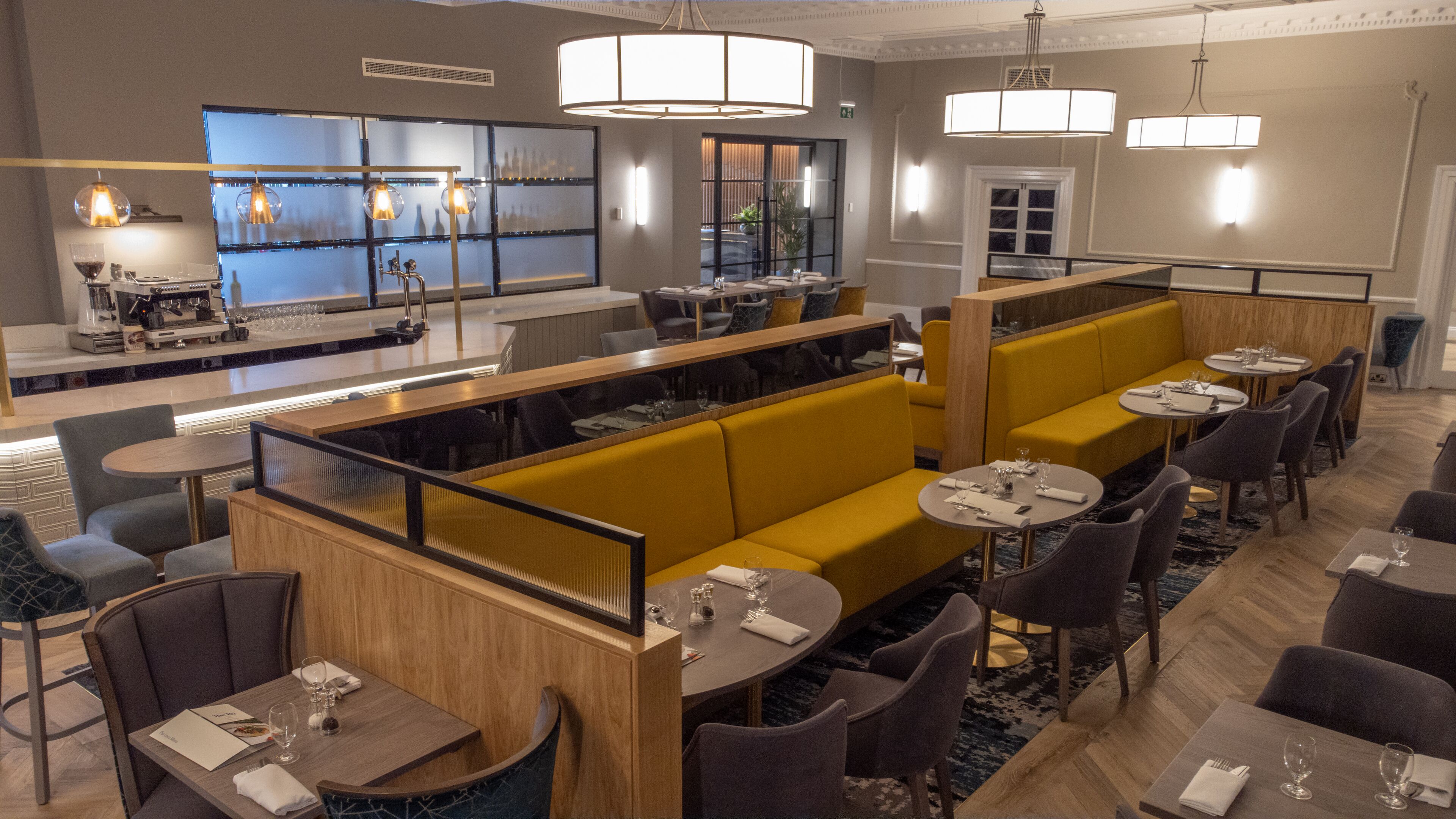 Un restaurant moderne avec des banquettes jaunes, des tables rondes et un coin bar.