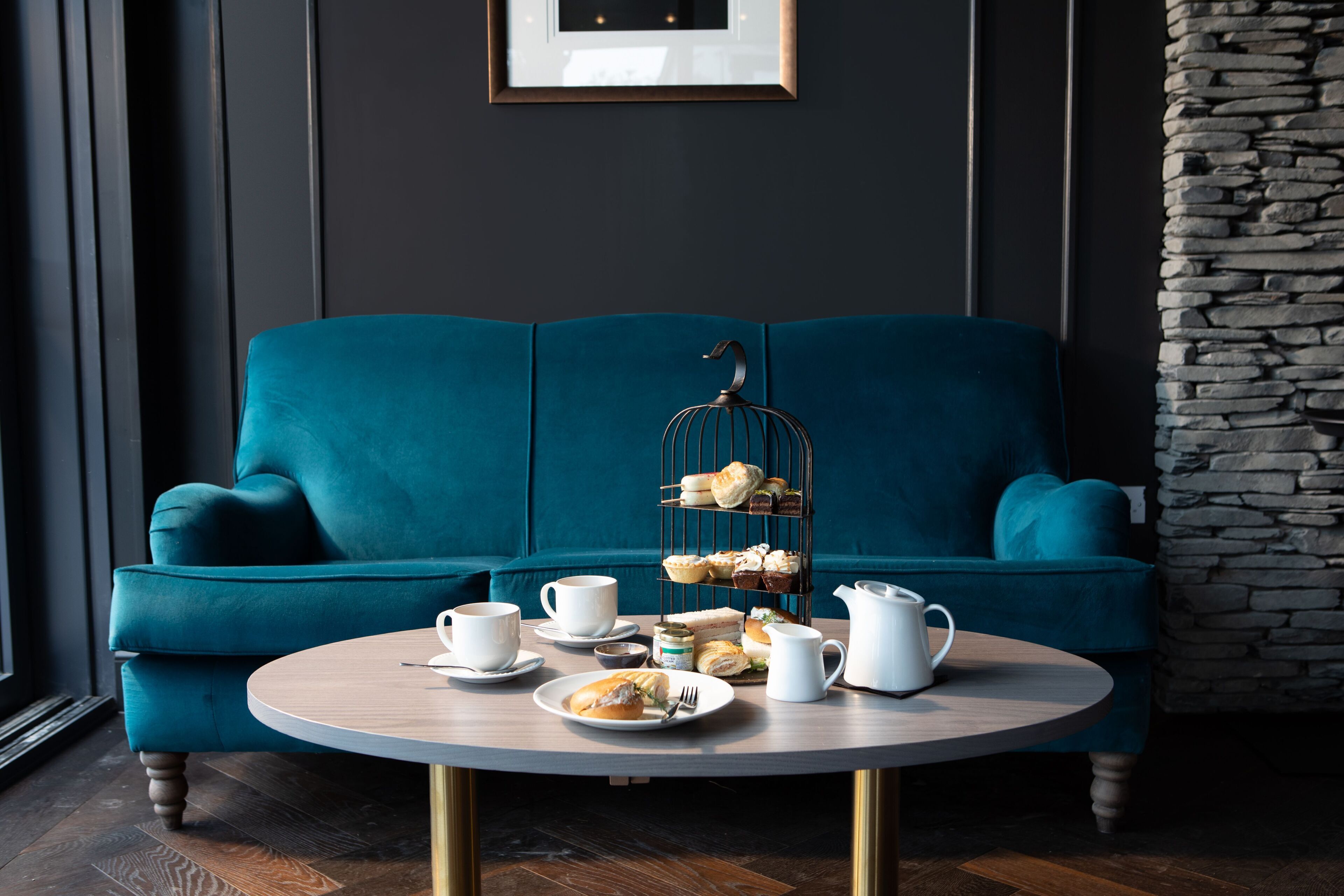 A teal sofa, a round table with a tea set, and a wire fruit basket.