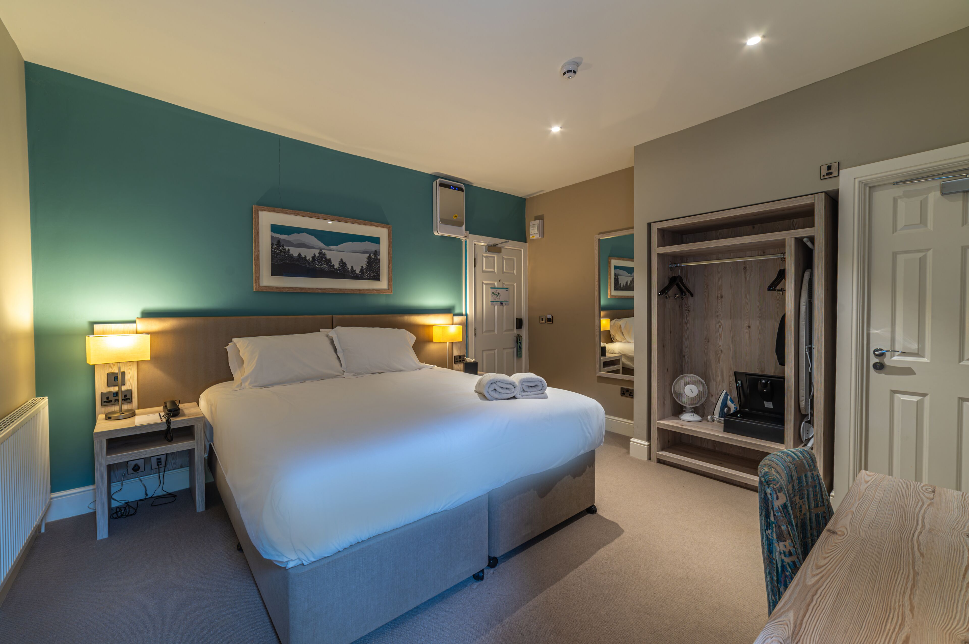 Une chambre à coucher bien rangée, avec un lit, des lampes de chevet, une armoire et un miroir.
