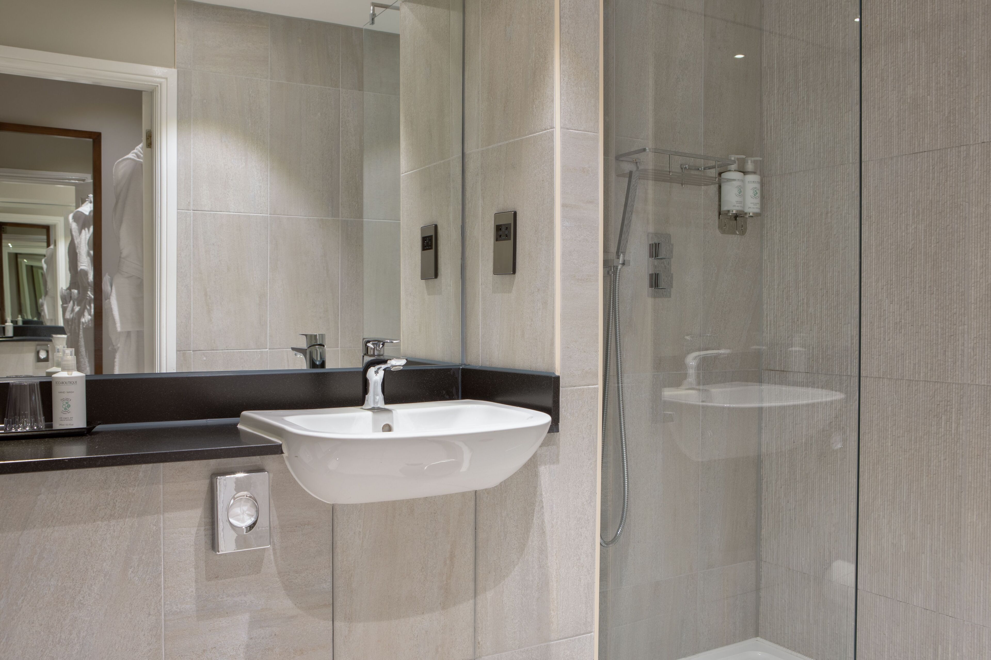 Une salle de bain moderne avec un grand miroir, un lavabo blanc et une douche séparée par une paroi de verre.