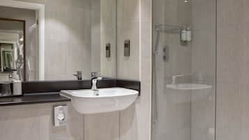 Une salle de bain moderne avec un grand miroir, un lavabo blanc et une douche séparée par une paroi de verre.