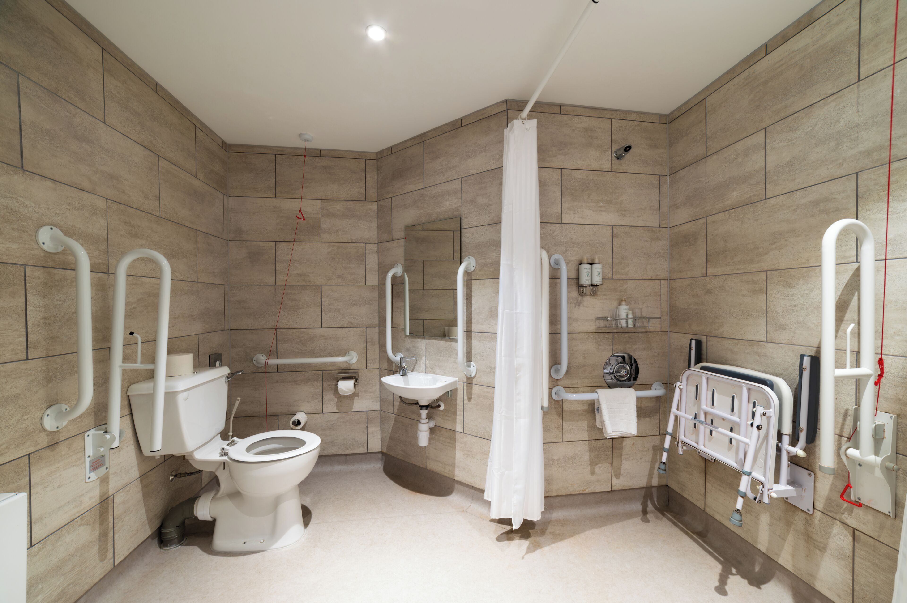 A modern bathroom with a toilet, sink, shower, and grab bars.