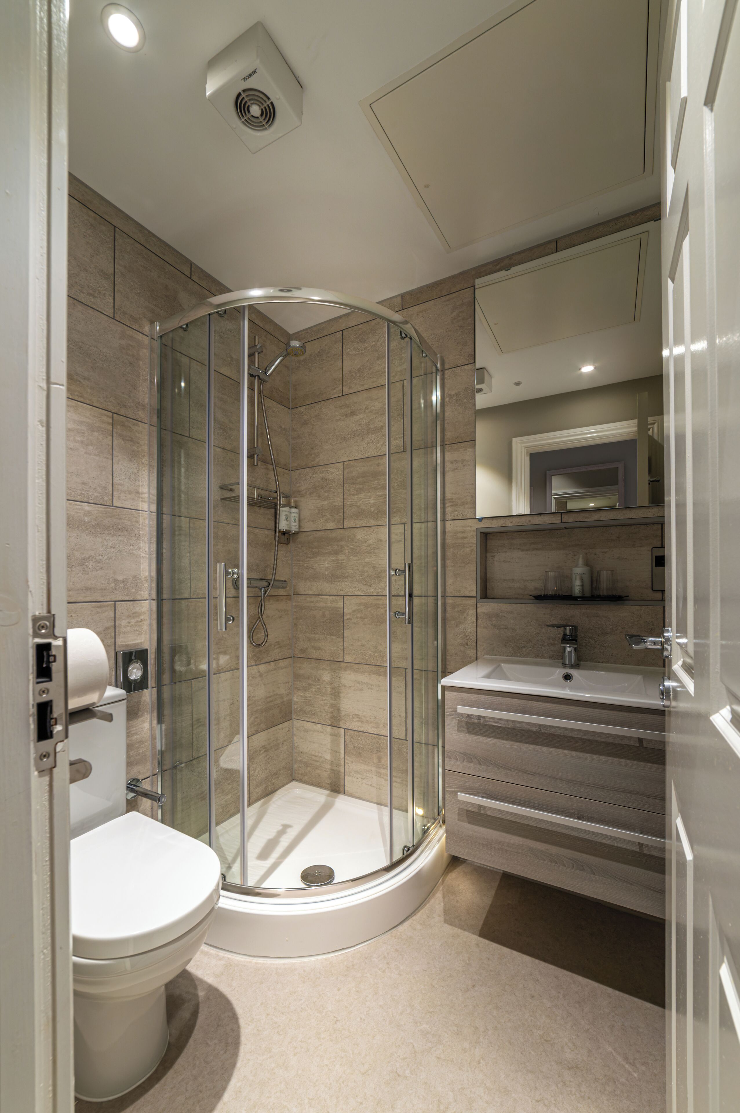 Une salle de bain moderne avec une douche à parois de verre, des toilettes blanches et un meuble-lavabo doté d’un miroir et d’étagères.