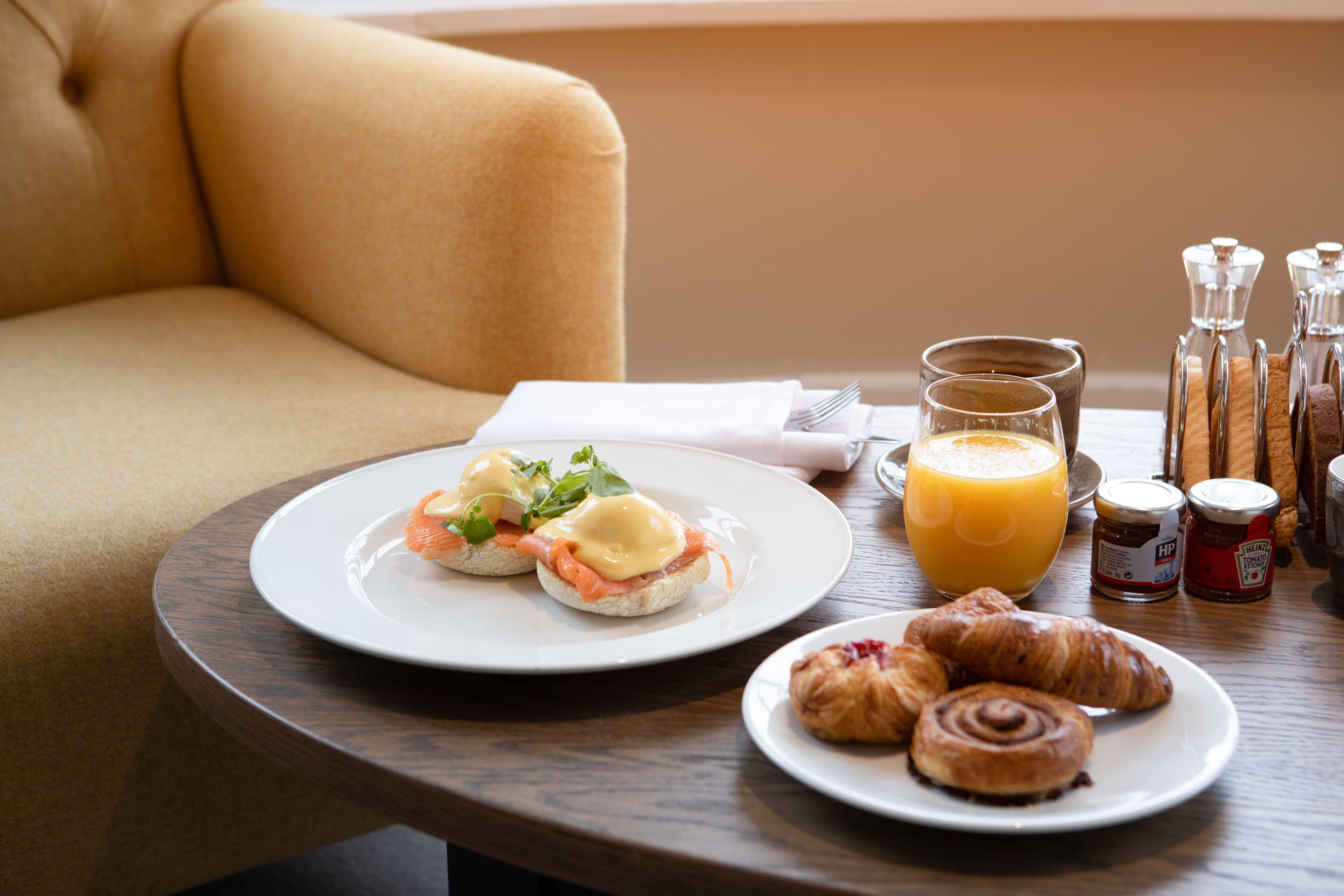 En frukostuppläggning med ägg Benedict, croissanter och apelsinjuice på ett träbord.