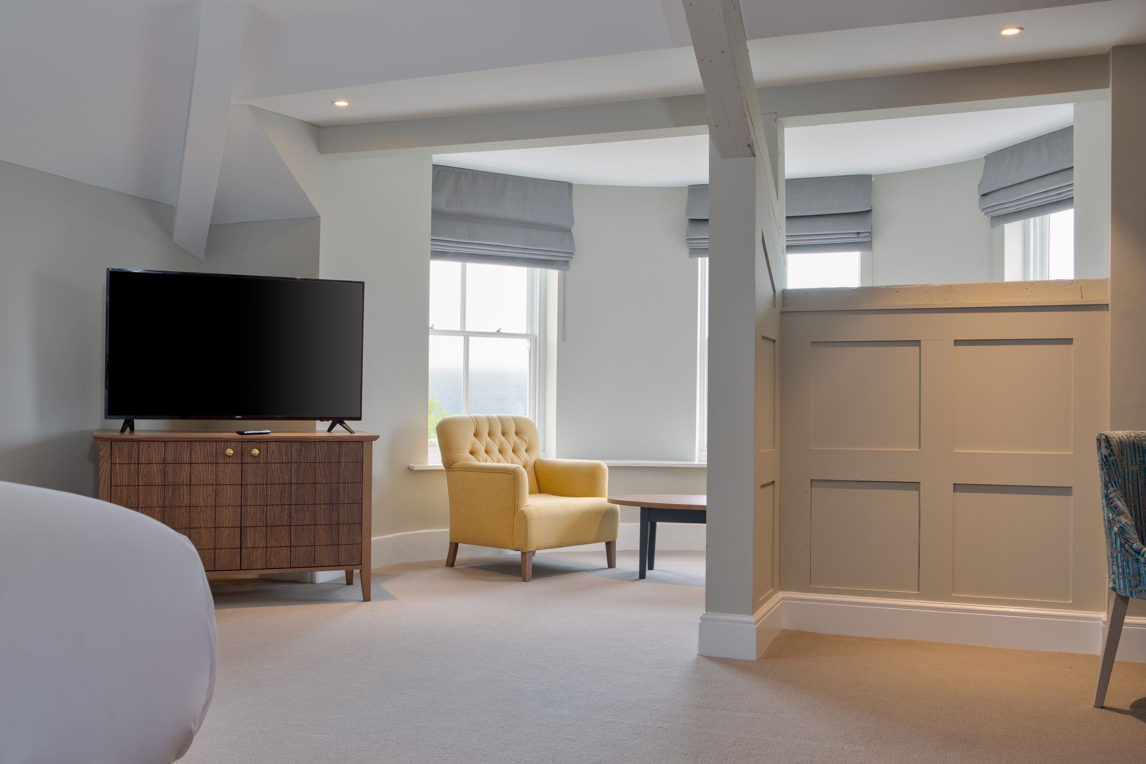 A modern bedroom with a flat-screen TV, a tufted armchair, a wooden cabinet, and a large wardrobe.