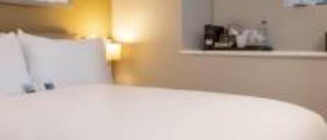 A hotel room with a bed, a nightstand, a window, and a painting on the wall.