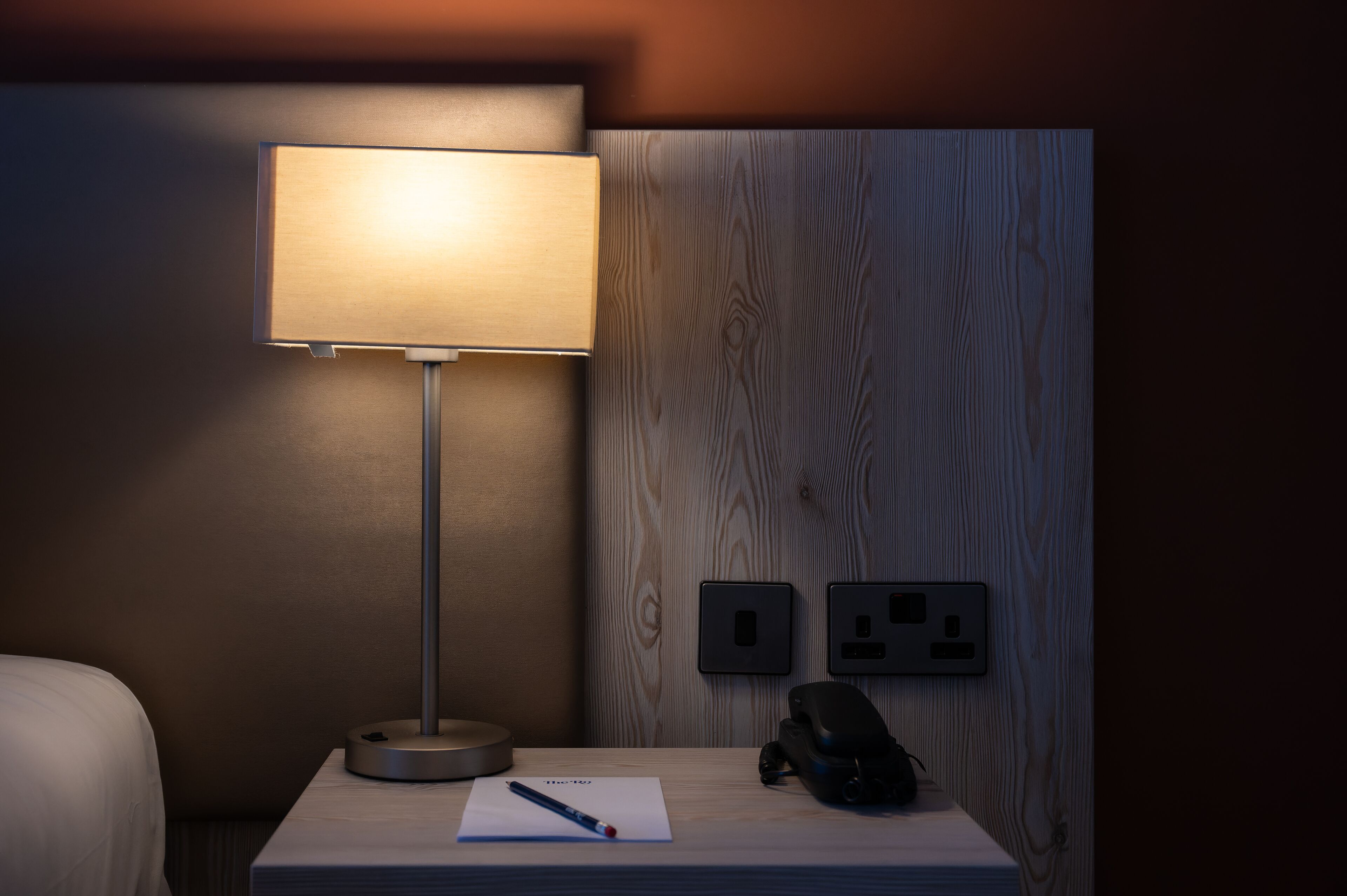 Una habitación de hotel con mesita de noche, lámpara, bloc de notas y teléfono.