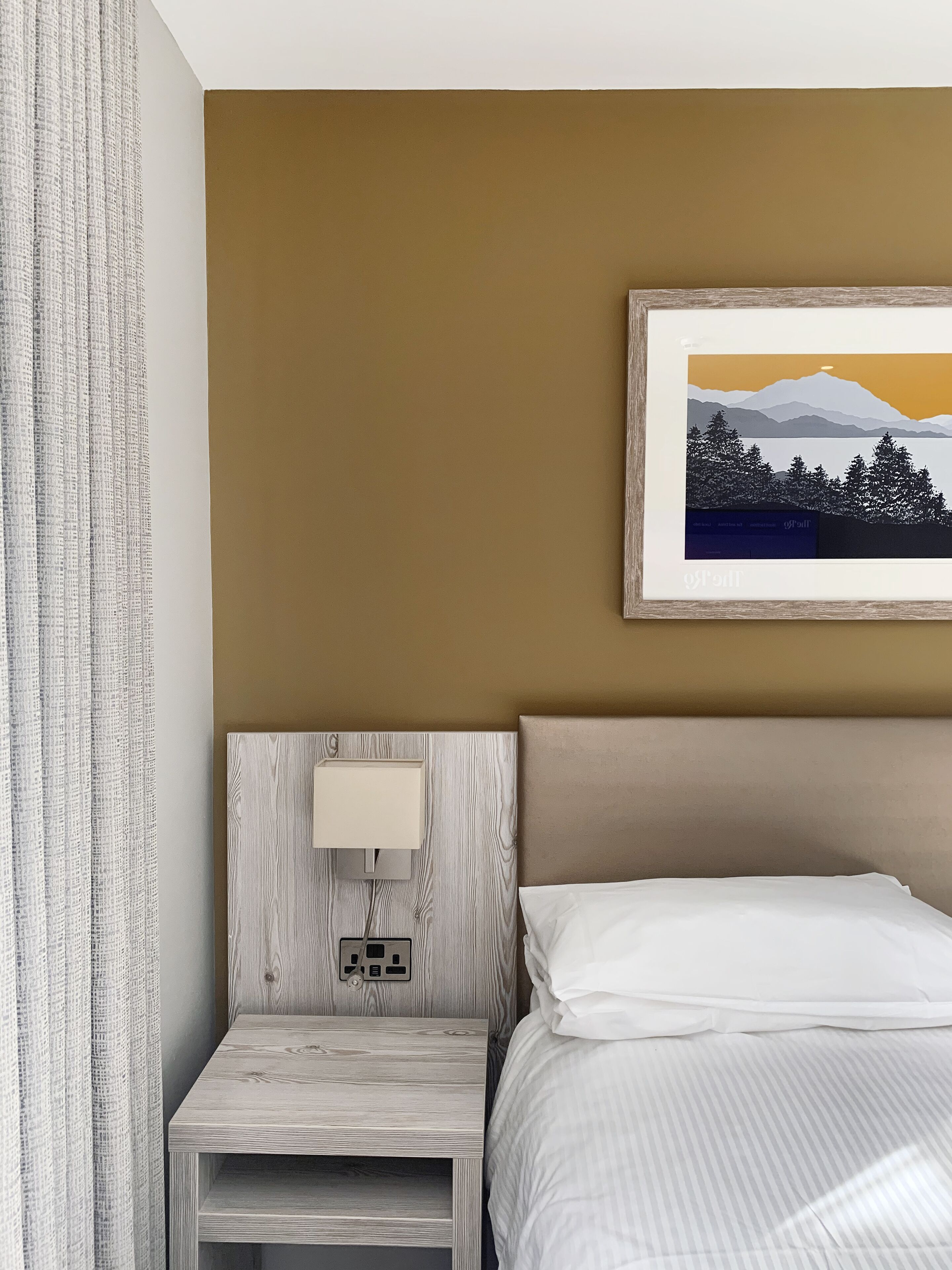 A hotel room with a bed, a nightstand with a lamp, and a framed picture on the wall.