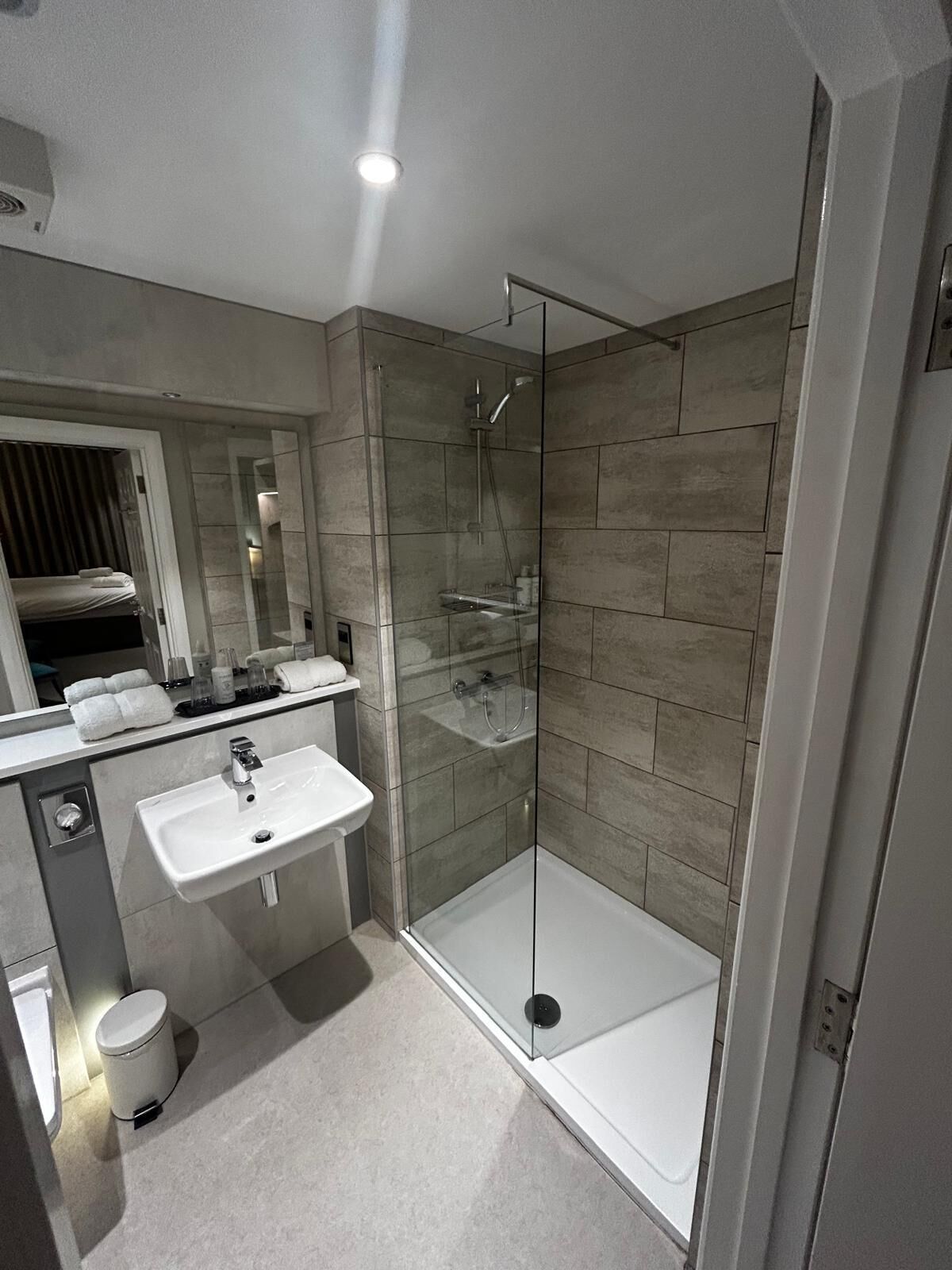A modern bathroom with a glass-enclosed shower, a white sink, and a mirror above the sink.
