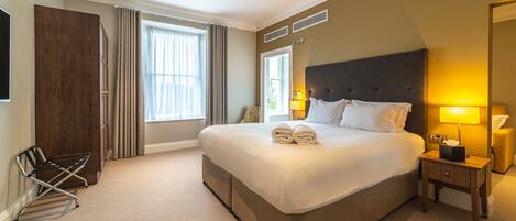 Een hotelkamer met een groot bed, een nachtkastje met lamp, een kledingkast en een raam met gordijnen.