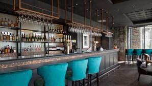 Zona de bar con una barra larga, varias estanterías llenas de botellas y varios taburetes.