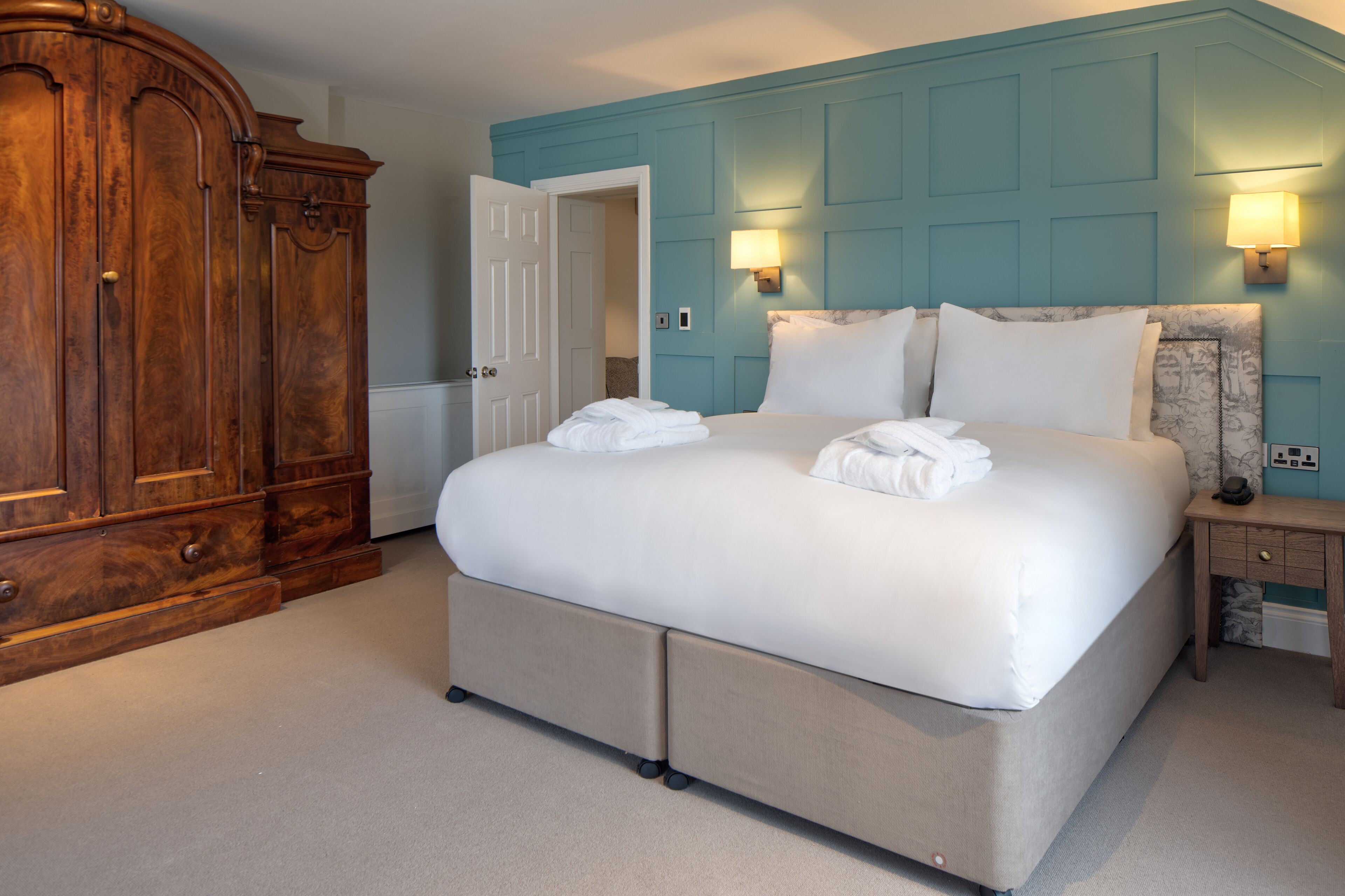 A bedroom with a large bed, a wardrobe, and two wall-mounted lamps.