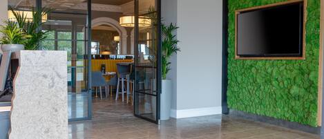 Een modern interieur met een glazen deur naar een eetgedeelte, een groen structuurwand en een wandgemonteerde flatscreen televisie.