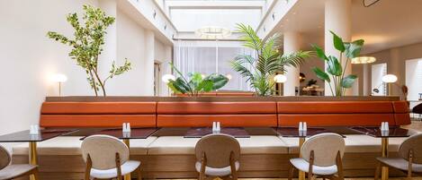 A modern hotel lobby with a central seating area, wooden flooring, and large windows allowing natural light.