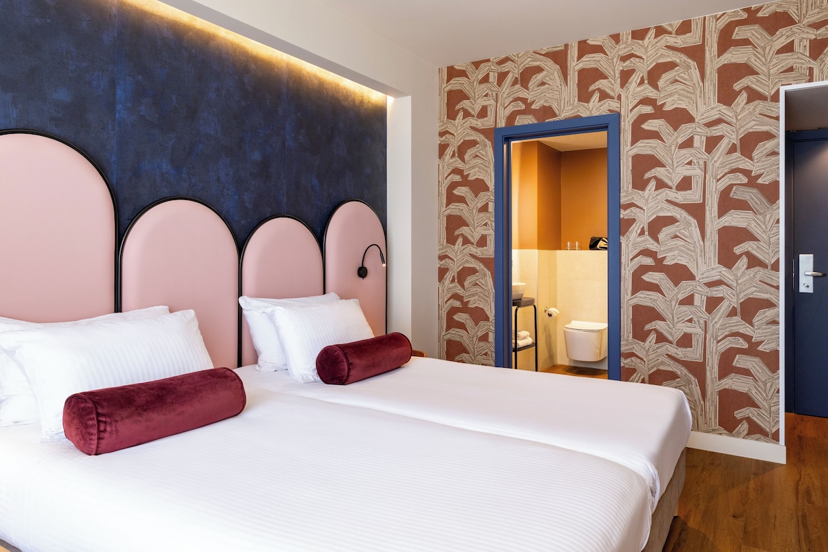 Ein Hotelzimmer mit Bett, Kopfteil, Bad mit Toilette und Waschbecken sowie einer Wand mit Muster.