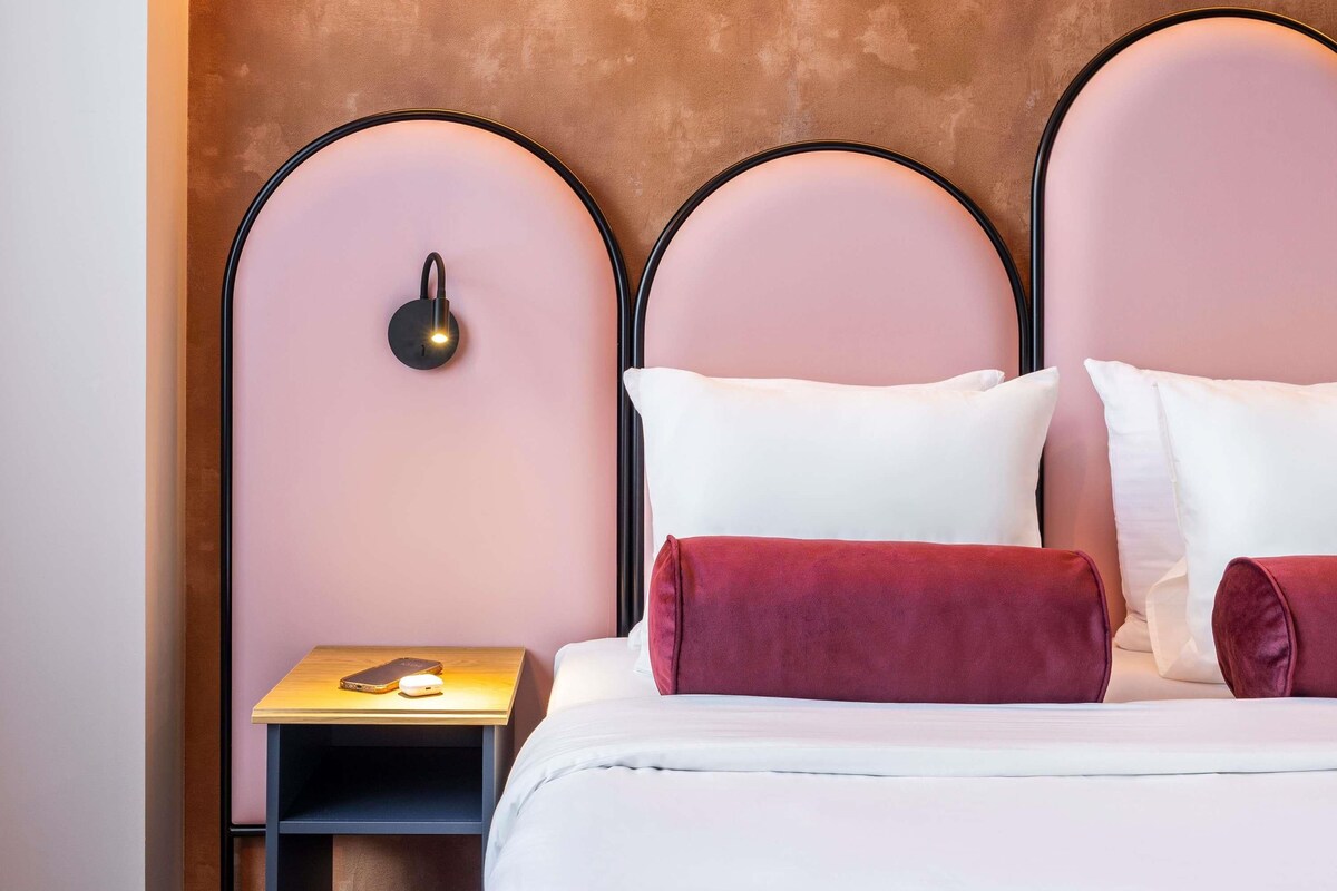 Une chambre d’hôtel avec un lit, des oreillers, une table de chevet avec un téléphone et une lampe fixée au mur.