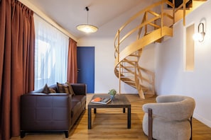 A modern living room with a sofa, a coffee table, a chair, a staircase, and a window with curtains. - Mercure Brussels Centre Rogier (Brussels)