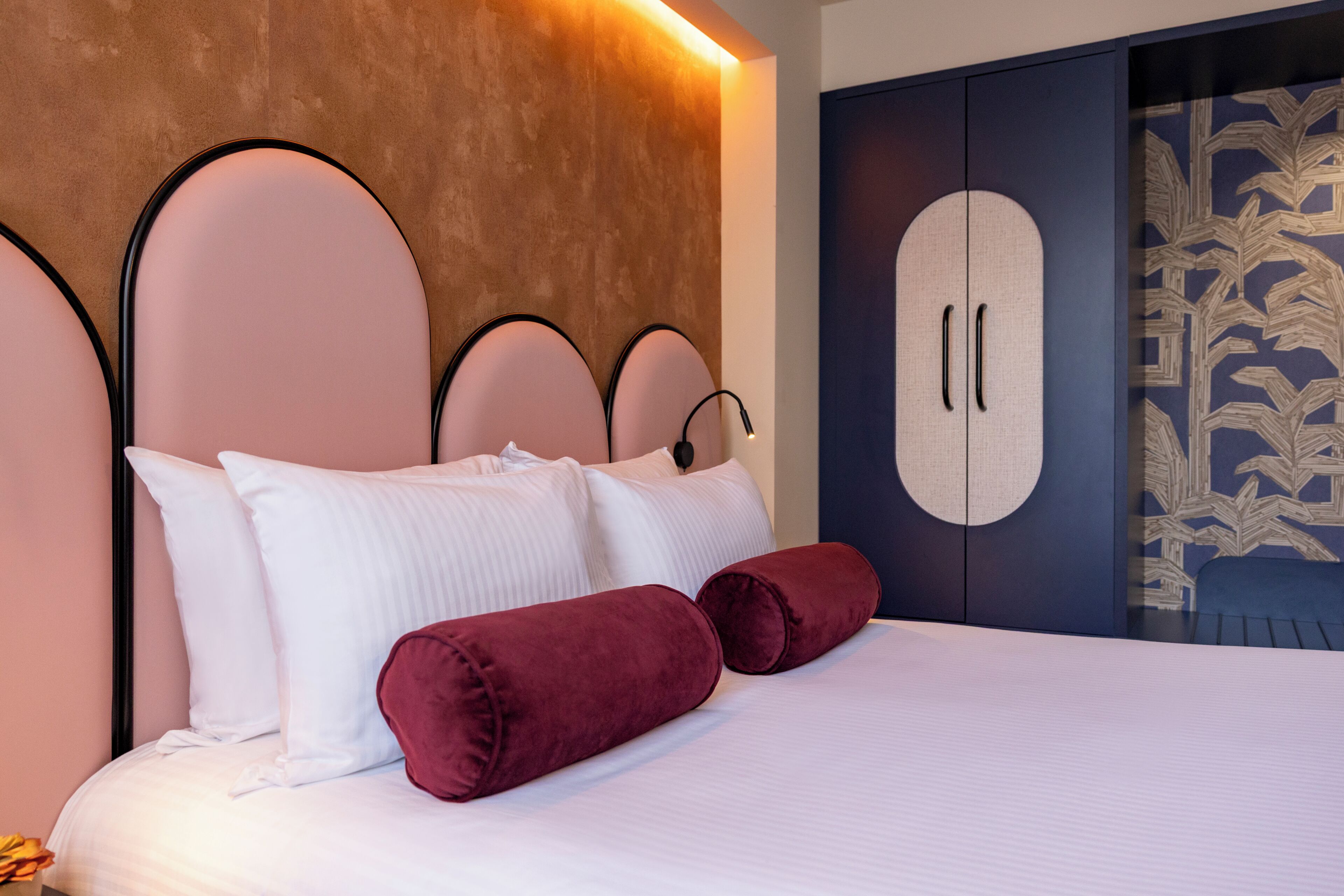 A bed with white bedding and two red pillows, a headboard with a circular design, and a wardrobe with a leaf pattern.