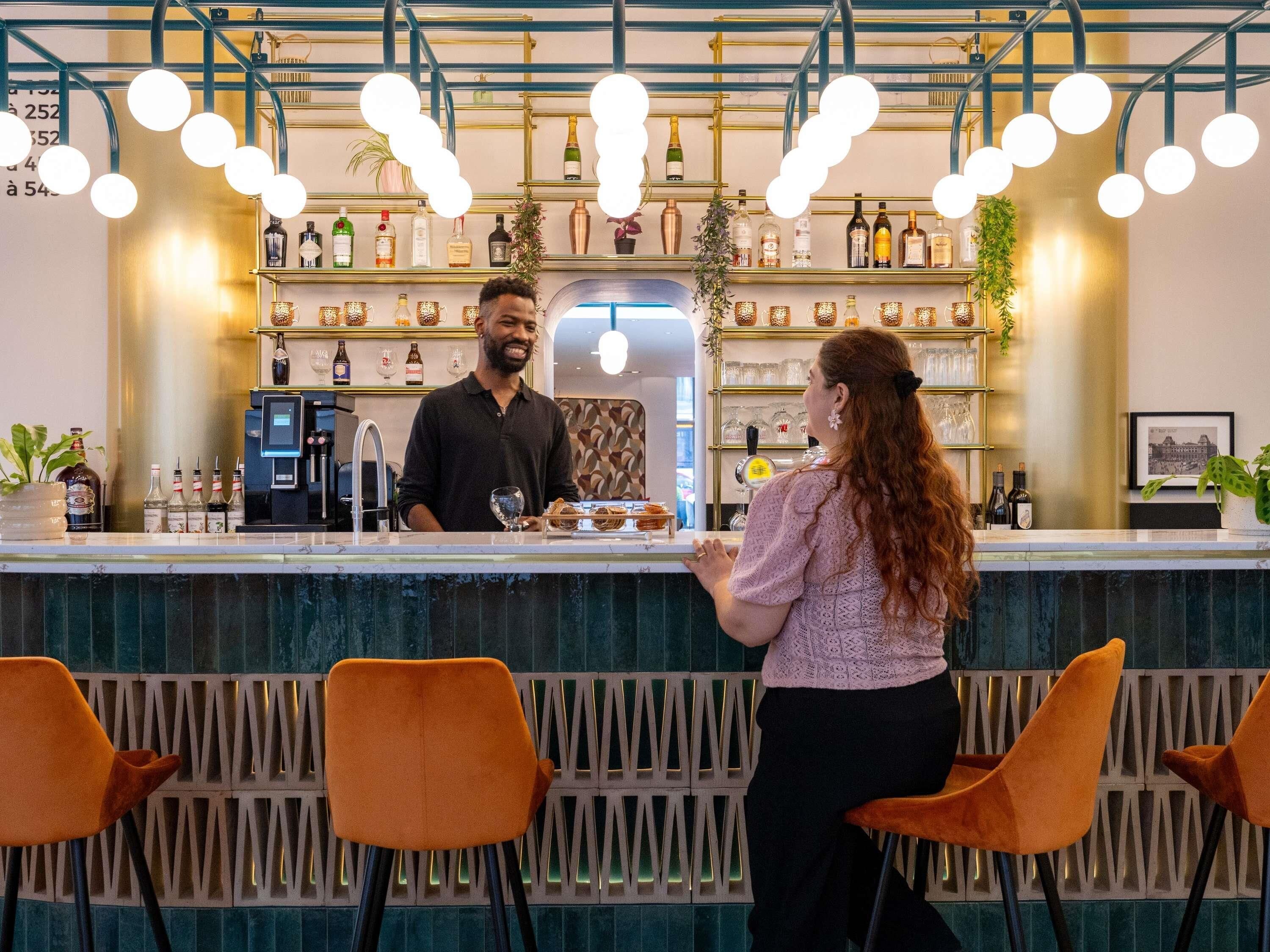 Zona de bar con mostrador, taburetes y estantes con botellas.