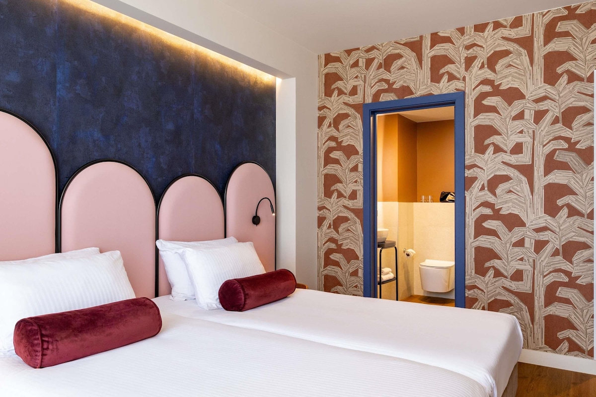 Ein Hotelzimmer mit Bett, Kopfteil, sichtbarem Badezimmer durch eine geöffnete Tür und strukturierter Wandtapete.