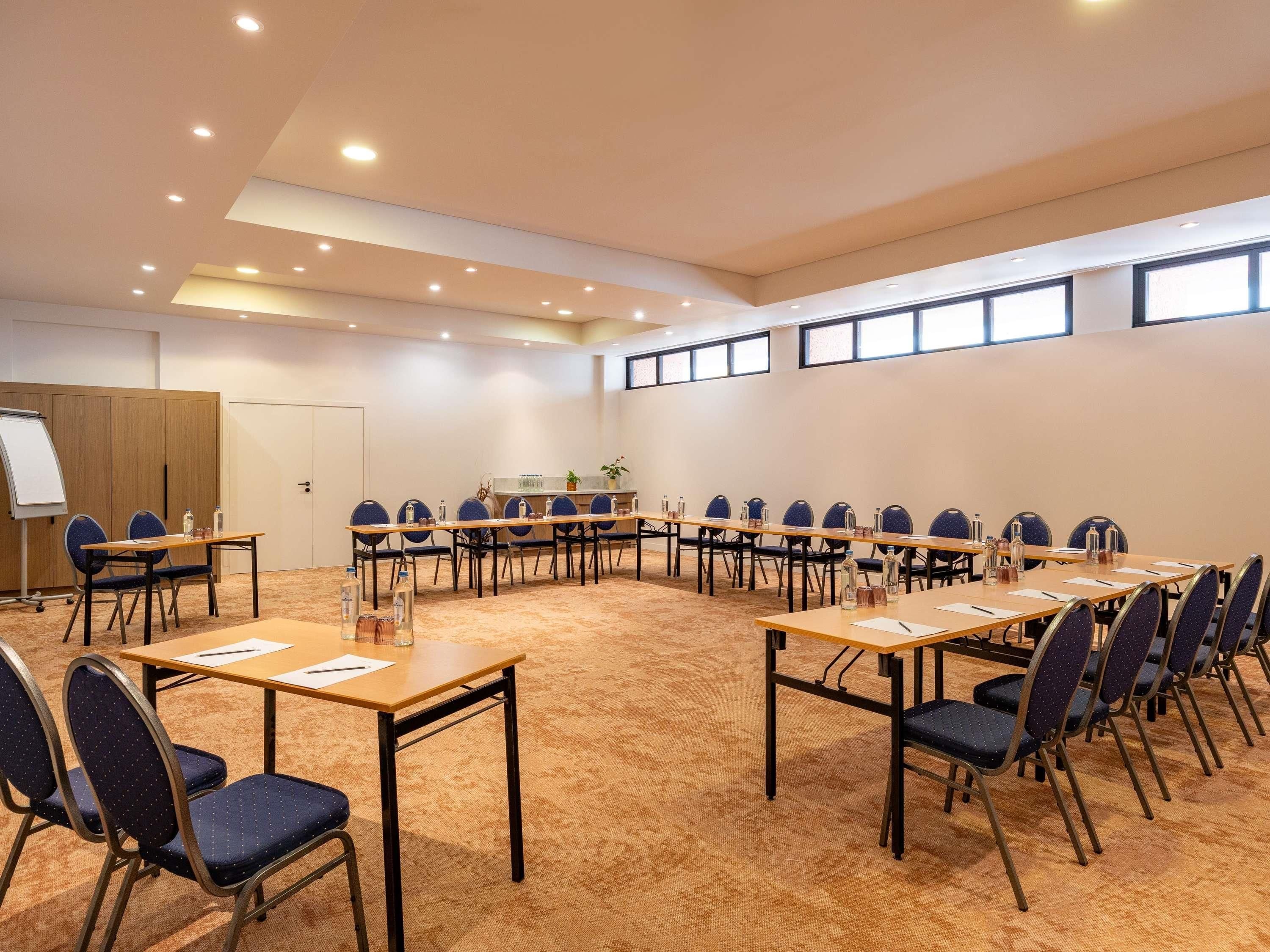 Un salón de conferencias con una mesa larga, sillas, una pizarra y suelo alfombrado.