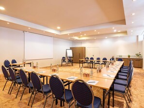 Un salón de conferencias con una larga mesa, sillas, una pantalla de proyector y una pizarra.