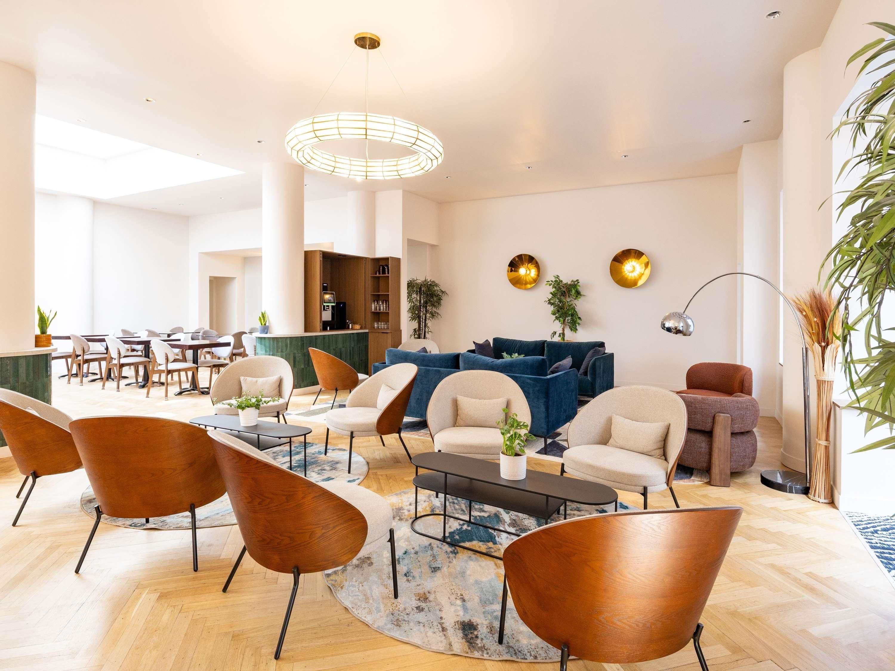 A modern hotel lobby with a reception desk, seating area with sofas and chairs, a coffee table, and a large window providing natural light.