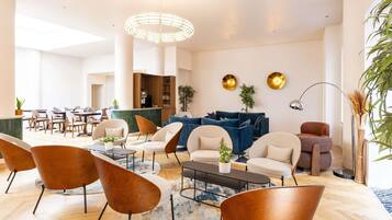 A modern hotel lobby with a reception desk, seating area with sofas and chairs, a coffee table, and a large window providing natural light.