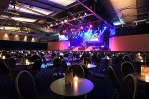 Um local de concertos com palco, assentos e mesas iluminadas por velas.