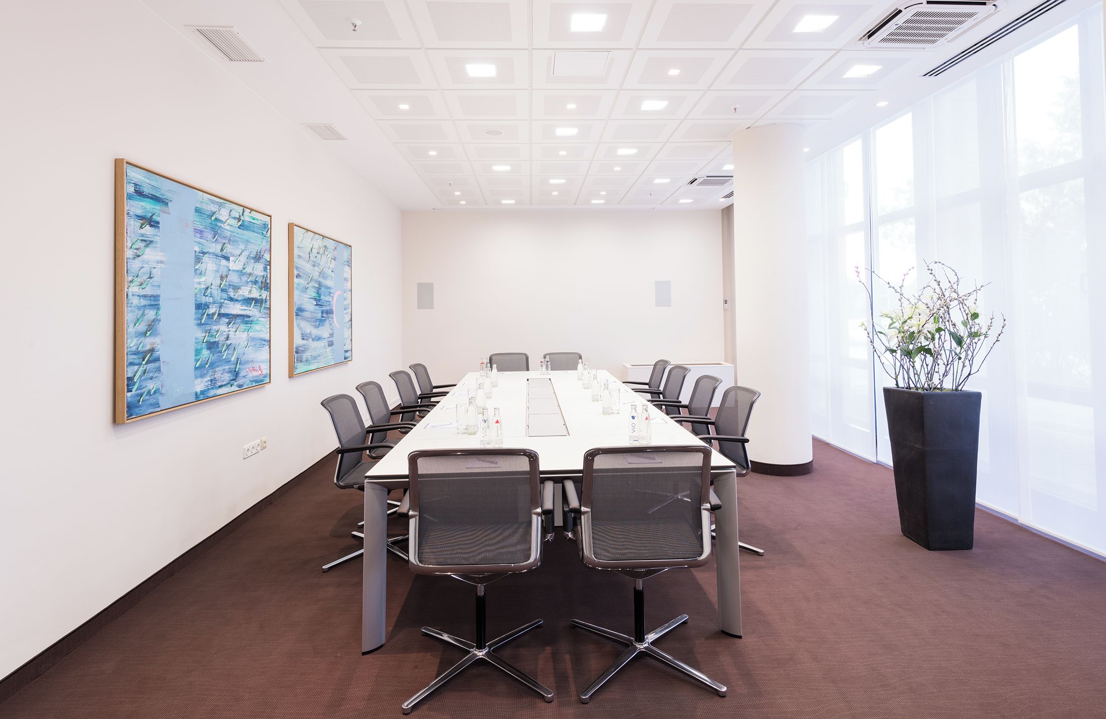 A conference room with a long table, chairs, and two abstract paintings on the wall.