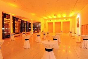 A spacious hall with multiple round tables, each with a white tablecloth and a black sash, arranged in rows. - Estrel Hotel Berlin (Berlin)