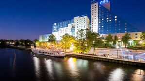 Ein Hotel mit moderner Glasfassade, einem Fluss davor und einem Boot, das an der Anlegestelle liegt.