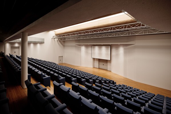 Un auditorio con filas de asientos, un escenario y una lámpara grande colgante.