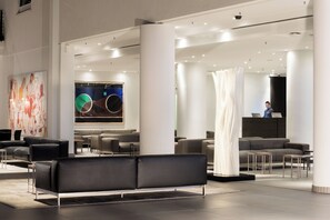 A modern lobby with a reception desk, seating area, and a large abstract painting. - Estrel Hotel Berlin (Berlin)