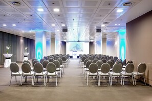 A conference room with rows of chairs facing a stage, equipped with a large screen and a podium. - Estrel Hotel Berlin (Berlin)