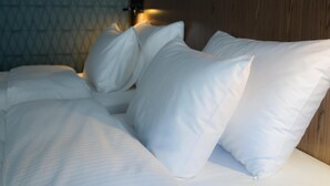 Una cama con sábanas y almohadas blancas, un cabecero de madera y un papel tapiz estampado al fondo.