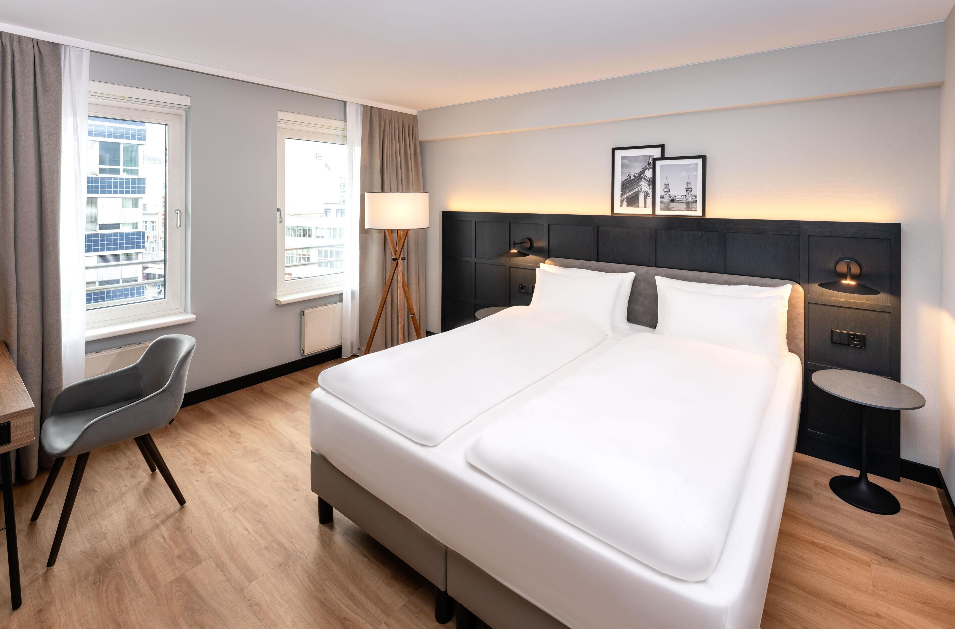 Hotellihuone, jossa on suuri sänky, työpöytä, tuoli sekä kaksi yöpöytää, joissa on lamput.
