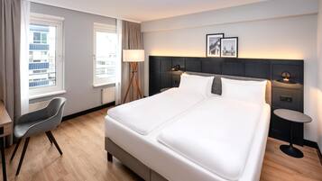 Habitación de hotel con una cama grande, un escritorio, una silla y dos mesitas de noche con lámparas.